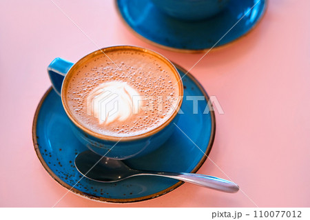 Cup of Cappuccino with Art Milk Foam Top View. Latte with Steel Spoon. Hot Coffee in a Blue Ceramic Mug With Saucer on a Pink Table. Modern Glamour Coffee Shop, Cafeteria. Thick Froth. No People. 4K Cup of Cappuccino with Art Milk Foam Top View. Latte with Steel Spoon. Hot Coffee in a Blue Ceramic Mug With Saucer on a Pink Table. Modern Glamour Coffee Shop, Cafeteria. Thick Froth. No People. 4K 110077012