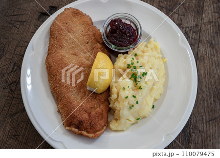 Pork escalope Viennese style from straw pork - in crispy breading served with homemade potato salad, lemon and cranberries. Pork escalope Viennese style from straw pork - in crispy breading served with homemade potato salad, lemon and cranberries. 110079475