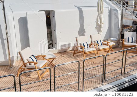 Close-up view of a relaxation area on the open teak deck of an expensive mega yacht at sunny day, with awnings stretched over the deck to protect from the sun, wealth life, table and chairs Close-up view of a relaxation area on the open teak deck of an expensive mega yacht at sunny day, with awnings stretched over the deck to protect from the sun, wealth life, table and chairs 110081322