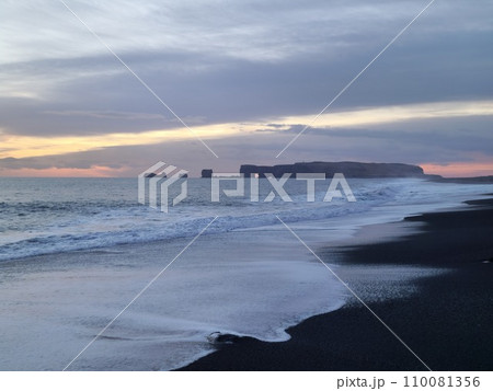 Natural black sand beach at sunset, spectacular coastline with waves crashing on atlantic ocean seashore. Icelandic wintry scenery with huge tides and freezing cold water, nordic nature. 110081356