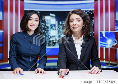Newscasters team read headlines live on television program, hosting night talk show filled with exclusive media information. Presenters team creating international reportage global issues. Newscasters team read headlines live on television program, hosting night talk show filled with exclusive media information. Presenters team creating international reportage global issues. 110081384