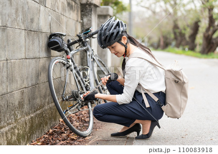 ロードバイクに 携帯用ポンプで空気を入れている若い女性 110083918