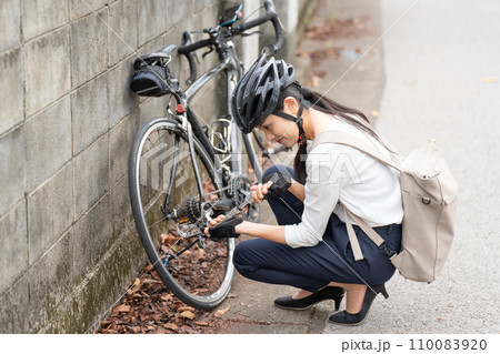 ロードバイクに 携帯用ポンプで空気を入れている若い女性 110083920
