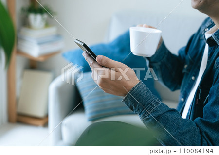 スマートフォンを見ながらカフェオレを飲む男性 110084194