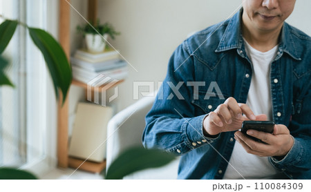 自宅でスマートフォンを操作するミドル男性 自宅でスマートフォンを操作するミドル男性 110084309