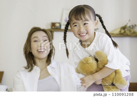 くまのぬいぐるみを持って飛び跳ねる4歳の女の子とそれをみて笑う茶髪の若いママ 110091208