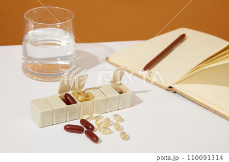 A glass of water, a daily pill box and dietary supplements on a white background. Adding dietary supplements to daily diet helps your body provide enough nutrients. 110091314
