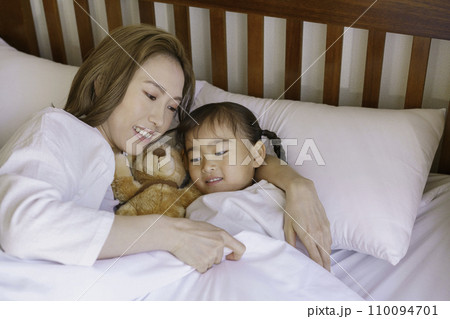 ベッドで女の子を寝かしつける茶髪の若いママ ベッドで女の子を寝かしつける茶髪の若いママ 110094701