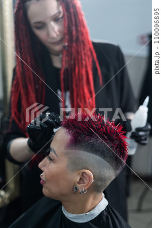 The hairdresser removes excess dye from the skin of a female with a cotton pad.Asian woman with a short haircut in a hairdressing salon. 110096895