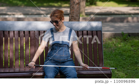 Blind red-haired pregnant woman sitting on a bench outdoors.  110096896