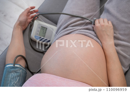 Close-up of the belly of a pregnant woman measuring blood pressure with a tonometer. Hypotension. Close-up of the belly of a pregnant woman measuring blood pressure with a tonometer. Hypotension. 110096959