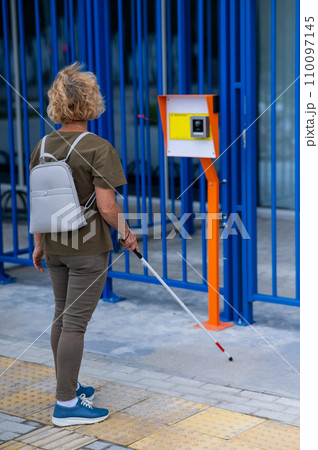 An elderly blind woman goes to a button to call help for people with disabilities. Vertical photo. An elderly blind woman goes to a button to call help for people with disabilities. Vertical photo. 110097145