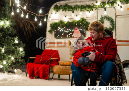Caucasian red-haired man with a boy in his arms at the mobile home. Father and son celebrate Christmas on a trip. Caucasian red-haired man with a boy in his arms at the mobile home. Father and son celebrate Christmas on a trip. 110097331