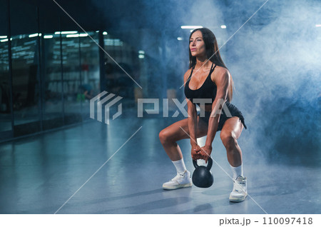 Caucasian woman squats with kettlebell in the gym.  110097418