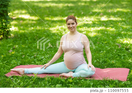Pregnant caucasian woman doing yoga in the park. Lateral tilt. Pregnant caucasian woman doing yoga in the park. Lateral tilt. 110097555