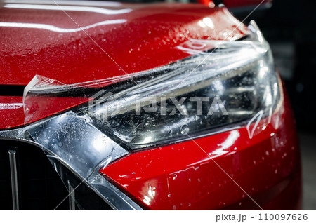 Close-up of a red car headlight with vinyl wrap.  110097626