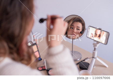 Caucasian woman leads an online make-up lesson for herself on her mobile phone 110097666