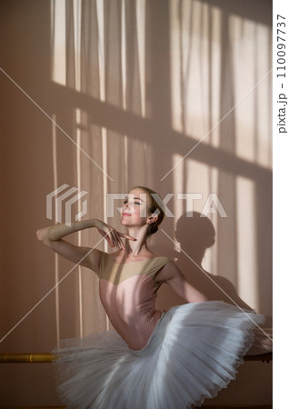 Beautiful graceful ballerina is practicing in the hall against the background of a window. Slender woman in tutu and pointe shoes in a dance class. Beautiful graceful ballerina is practicing in the hall against the background of a window. Slender woman in tutu and pointe shoes in a dance class. 110097737