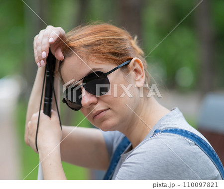 Blind red-haired woman sitting outdoors leaning on a cane.  110097821