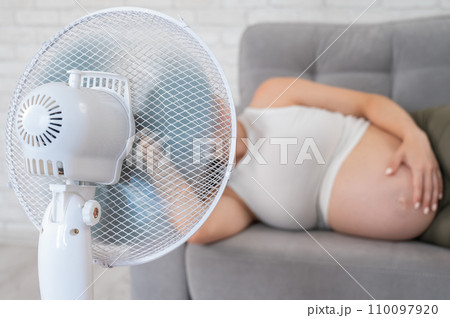 Pregnant woman suffers from heat and lies on the sofa near the electric fan.  110097920