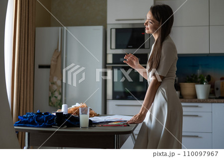 Woman drawing sketches of swimwear and underwear in watercolor while sitting in the kitchen.  110097967