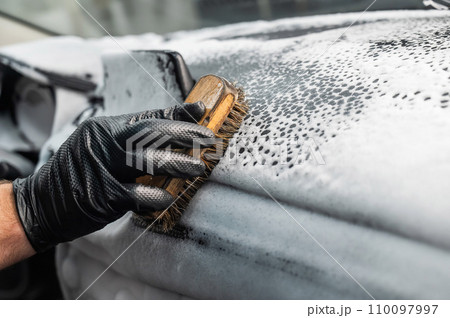 A mechanic cleans the interior of a car with a brush and foam. A mechanic cleans the interior of a car with a brush and foam. 110097997