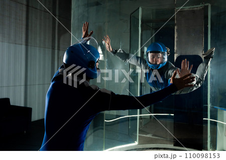 A male instructor teaches a woman how to fly in a wind tunnel. Free fall simulator. 110098153