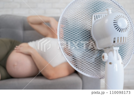 Pregnant woman suffers from heat and lies on the sofa near the electric fan. Pregnant woman suffers from heat and lies on the sofa near the electric fan. 110098173