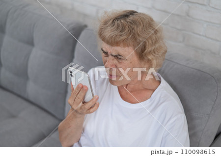 An elderly Caucasian woman suffers from myopia and tries to read a message on a smartphone. An elderly Caucasian woman suffers from myopia and tries to read a message on a smartphone. 110098615