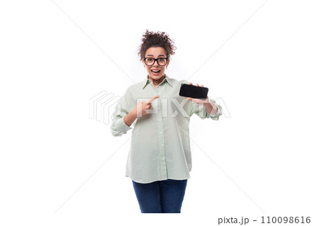 young pretty secretary woman with curly hair dressed in shirt shows smartphone screen with mockup 110098616
