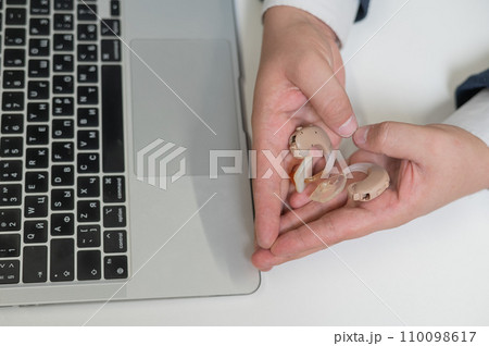 A man holds hearing aids and makes a heart shape with his hands. A man holds hearing aids and makes a heart shape with his hands. 110098617