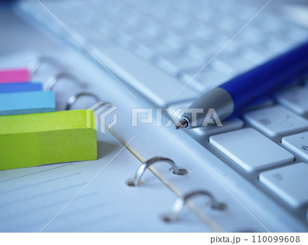 テーブルに置かれた手帳とキーボードと付箋 110099608