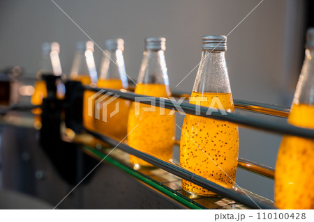 The beverage factory's automated bottling line efficiently fills transparent bottles with organic basil or chia seed drinks blended with pomegranate. Quality production and cleanliness are evident. 110100428