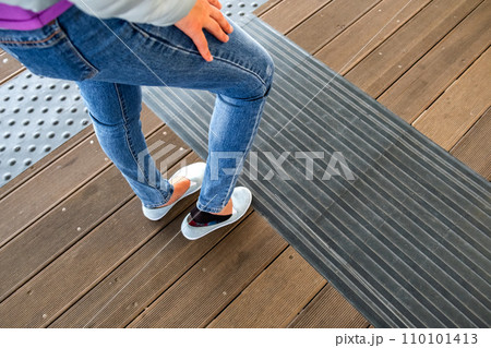 Female legs in denim jeans pants and light summer sneakers standing on wooden floow. Female legs in denim jeans pants and light summer sneakers standing on wooden floow. 110101413