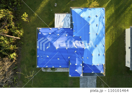 Top view of leaking house roof covered with protective tarp sheets against rain water leaks until replacement of asphalt shingles. Damage of building rooftop as aftermath of hurricane Ian in Florida Top view of leaking house roof covered with protective tarp sheets against rain water leaks until replacement of asphalt shingles. Damage of building rooftop as aftermath of hurricane Ian in Florida 110101464