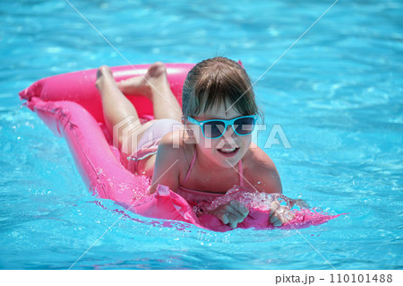 Happy child girl relaxing on inflatable air mattress in swimming pool on sunny summer day during tropical vacations. Summertime activities concept 110101488