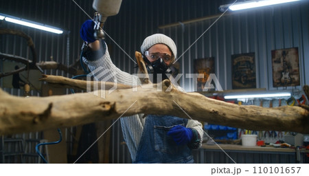 Creative female carpenter sprays liquid or wood varnish on tree branch 110101657