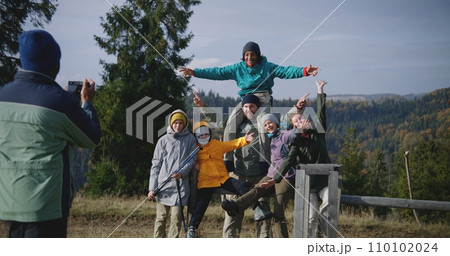 Diverse tourists smile and wave at camera standing against mountains landscape Diverse tourists smile and wave at camera standing against mountains landscape 110102024