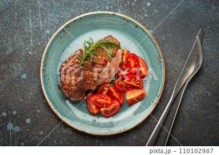 Delicious roasted duck breast fillet with golden crispy skin, with pepper and rosemary, top view on ceramic blue plate served with cherry tomatoes salad, rustic concrete rustic background Delicious roasted duck breast fillet with golden crispy skin, with pepper and rosemary, top view on ceramic blue plate served with cherry tomatoes salad, rustic concrete rustic background 110102987