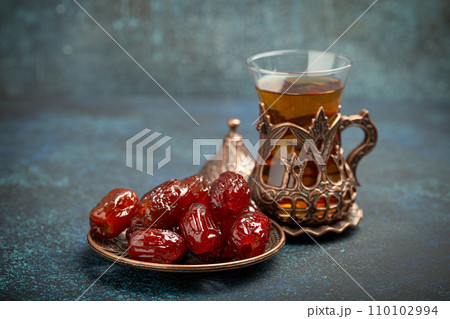 Breaking fasting with dried dates during Ramadan Kareem, Iftar meal with dates and Arab tea in traditional glass, angle view on rustic blue background. Muslim feast 110102994