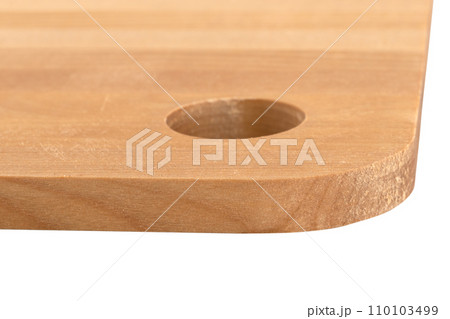 Close-up of the edge of a wooden cutting board with a round hole. 110103499