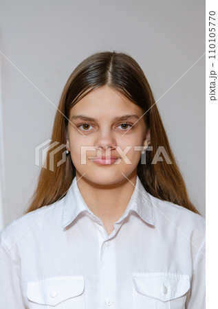 Portrait of a fourteen-year-old girl in a white shirt on a gray background 110105770