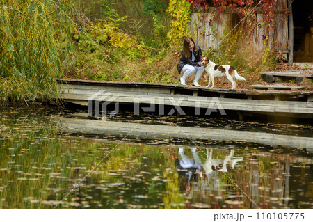 Young beautiful girl petting a dog near a lake in an autumn park 110105775
