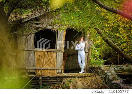 A young beautiful girl in white clothes stands near an old abandoned house in the forest 110105777