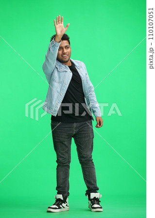 a full-length man on a green background waves hello 110107051