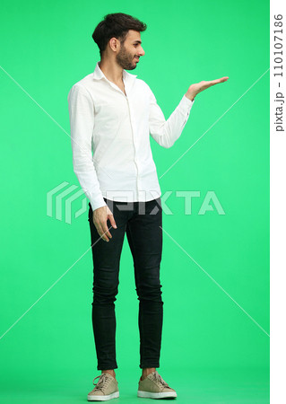A young man on a green background in full growth shows his hand to the side 110107186