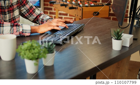 Employee remotely working from home on computer, inputing data in his brick wall apartment. African american freelancer typing on keyboard, teleworking at nice clean wooden desk, close up Employee remotely working from home on computer, inputing data in his brick wall apartment. African american freelancer typing on keyboard, teleworking at nice clean wooden desk, close up 110107799