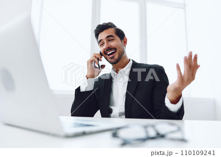 Man in office businessman sitting at desk and working in laptop and talking on phone, modern suit, finance and startup concept and data analysis, working lifestyle in bright office. Man in office businessman sitting at desk and working in laptop and talking on phone, modern suit, finance and startup concept and data analysis, working lifestyle in bright office. 110109241