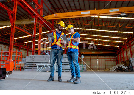 Wide shot of two Caucasian technician workers hold tablet and stand together to discuss about work in factory workplace area. Wide shot of two Caucasian technician workers hold tablet and stand together to discuss about work in factory workplace area. 110112712