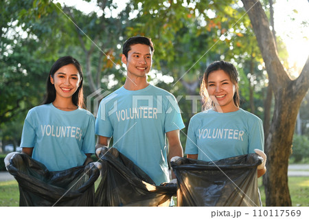 Group of young volunteers with garbage bags cleaning up nature in sunny day. Charity and ecology concept. 110117569